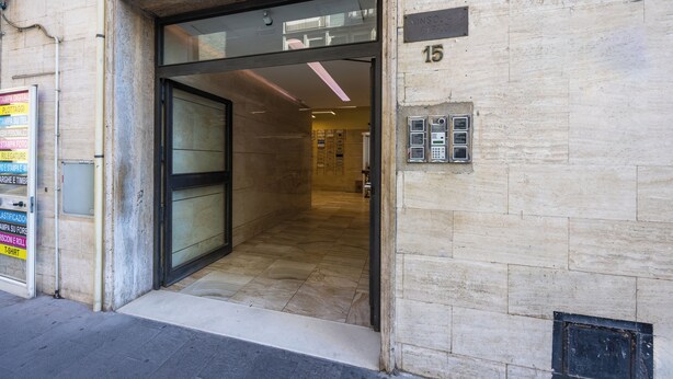 Entrada de un hotel con puerta de vidrio, piso de baldosas y un cartel que indica el número 15.