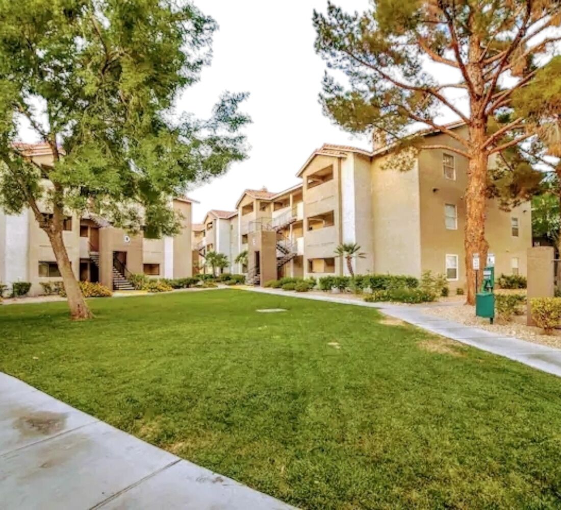 A courtyard with a well-maintained lawn, trees, and a building with multiple balconies and a central staircase.