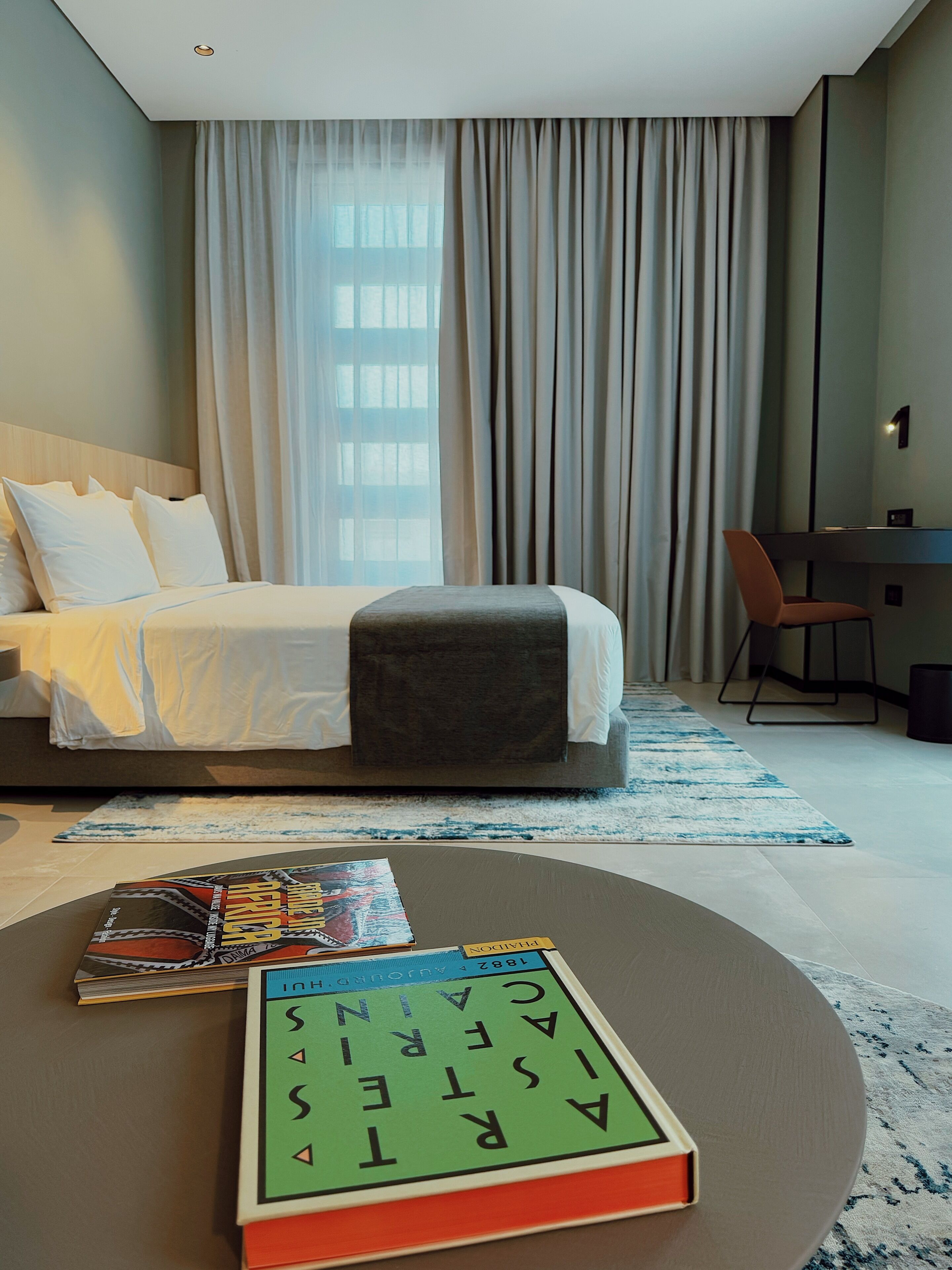 A hotel room with a bed, a desk, and a coffee table with books.