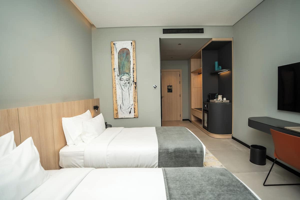A hotel room with two beds, a desk, a TV, and a painting on the wall.