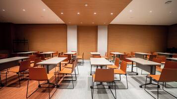 A conference room with tables and chairs, wooden walls, and ceiling lights.