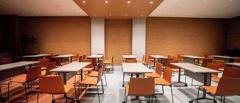 A conference room with tables and chairs, wooden walls, and ceiling lights.