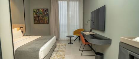 A modern hotel room with a bed, a desk, a chair, a TV, and a painting on the wall.