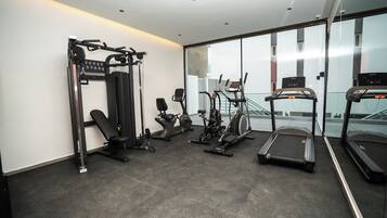 A modern gym with various exercise equipment, including a bench press, elliptical, stationary bike, and treadmills.