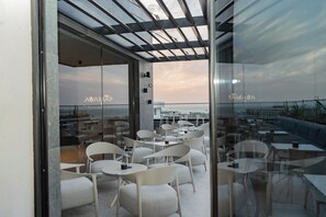 A rooftop terrace with glass walls, white chairs, and tables, offering a view of the cityscape. - Sama Hotels (Dakar)