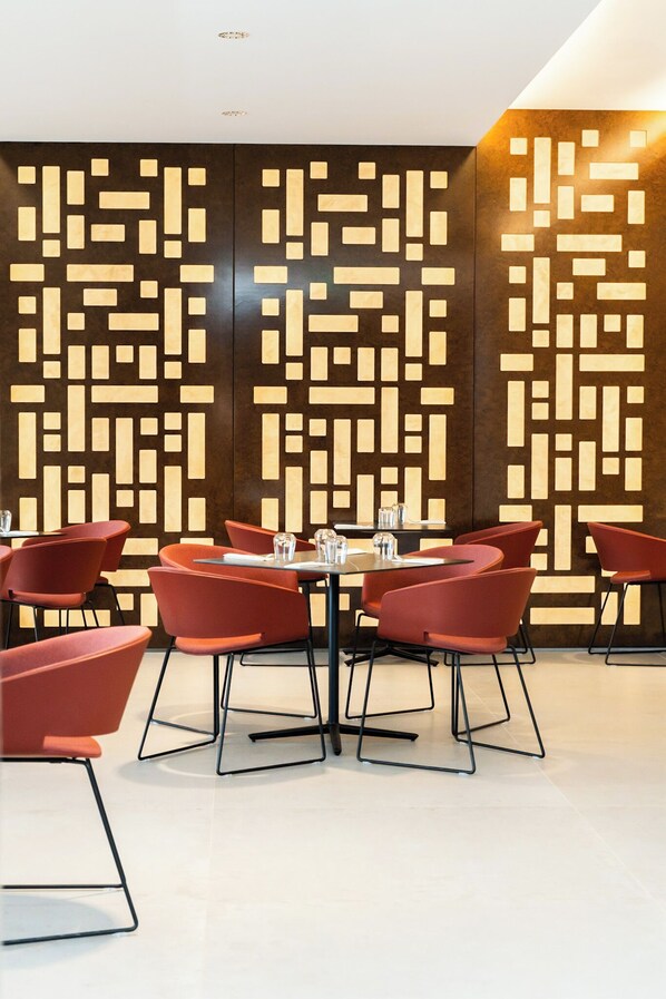 Un espace de restauration moderne avec des chaises et des tables rouges, un motif géométrique sur le mur et une esthétique épurée et minimaliste.