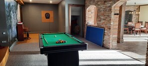 Ein Billardtisch in einem Raum mit Dartscheibe, einem Holzstuhl und einer Ziegelwand.