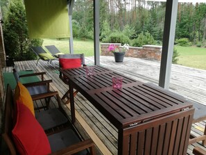 A wooden deck with a table and chairs, a green wall, and a view of a garden. - Forest apartment in the loop of the river Neris (Verkšionys)