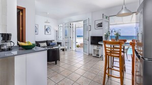 Una cocina moderna con una isla central, un comedor con vistas al mar y una sala de estar con sofá y televisor.