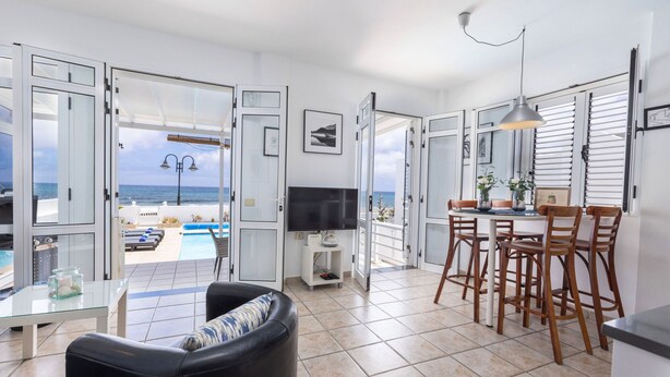 Una sala de estar moderna con televisor, comedor y vista al mar.