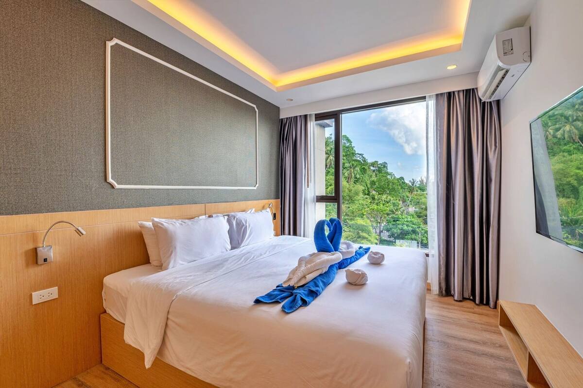 A hotel room with a large bed, a view of greenery, and a modern design.