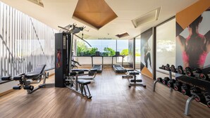 A gym with exercise equipment, large windows, and a view of greenery. - Aristo 2 Phuket by RESAVA (Choeng Thale)