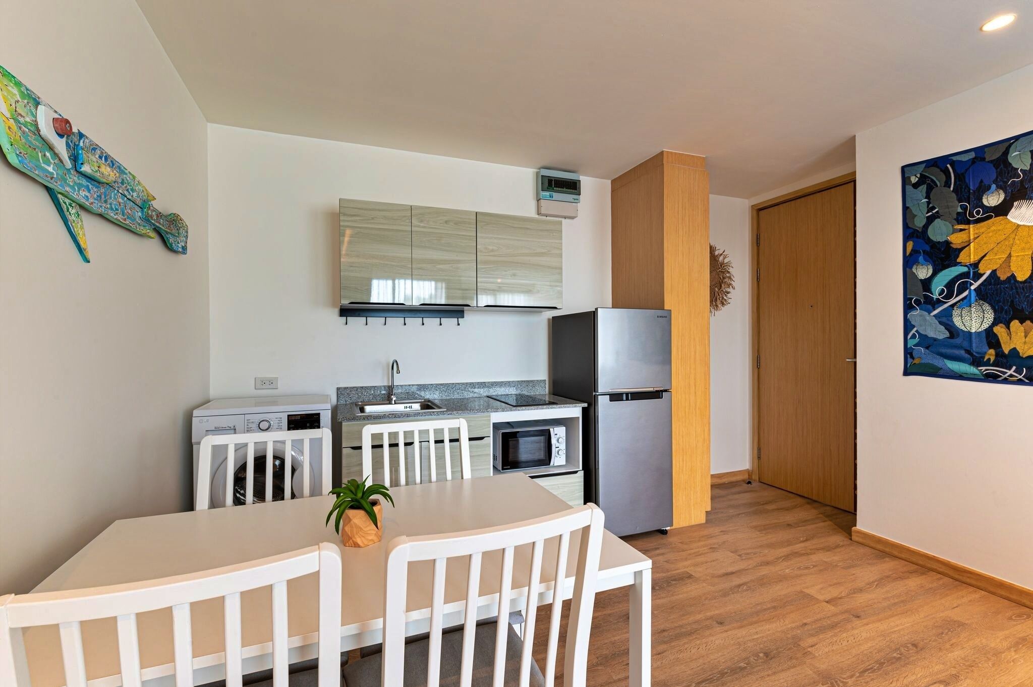 A compact kitchen with a microwave, oven, and refrigerator. There is a dining table with chairs and a washing machine.