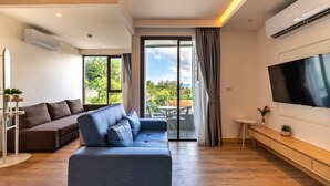 A modern living room with a sofa, a TV, and a balcony with a view. - Aristo 2 Phuket by RESAVA (Choeng Thale)