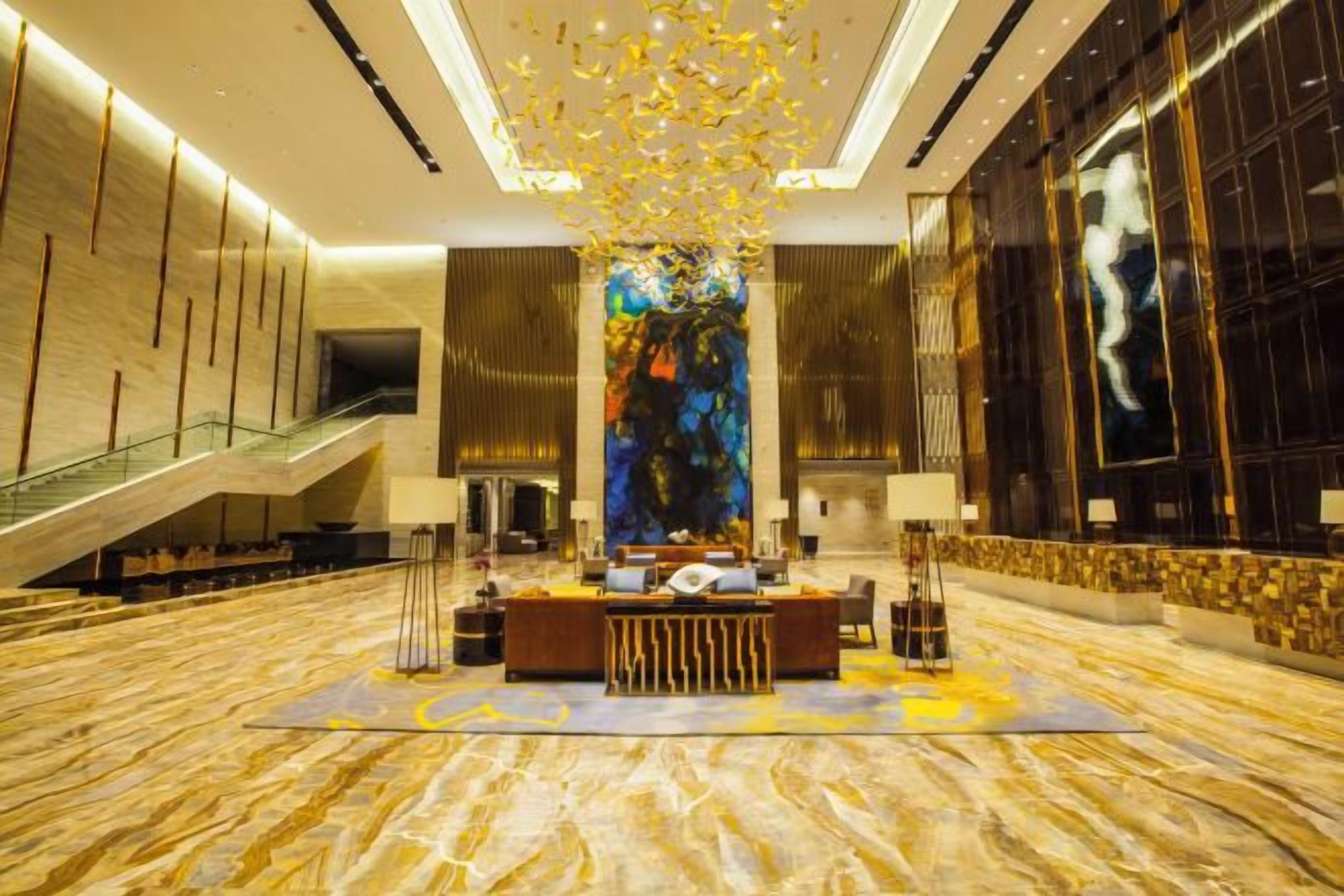 Eine geräumige Lobby mit einer zentralen Rezeption, einer Treppe und einem großen, abstrakten Kunstwerk an der Wand.