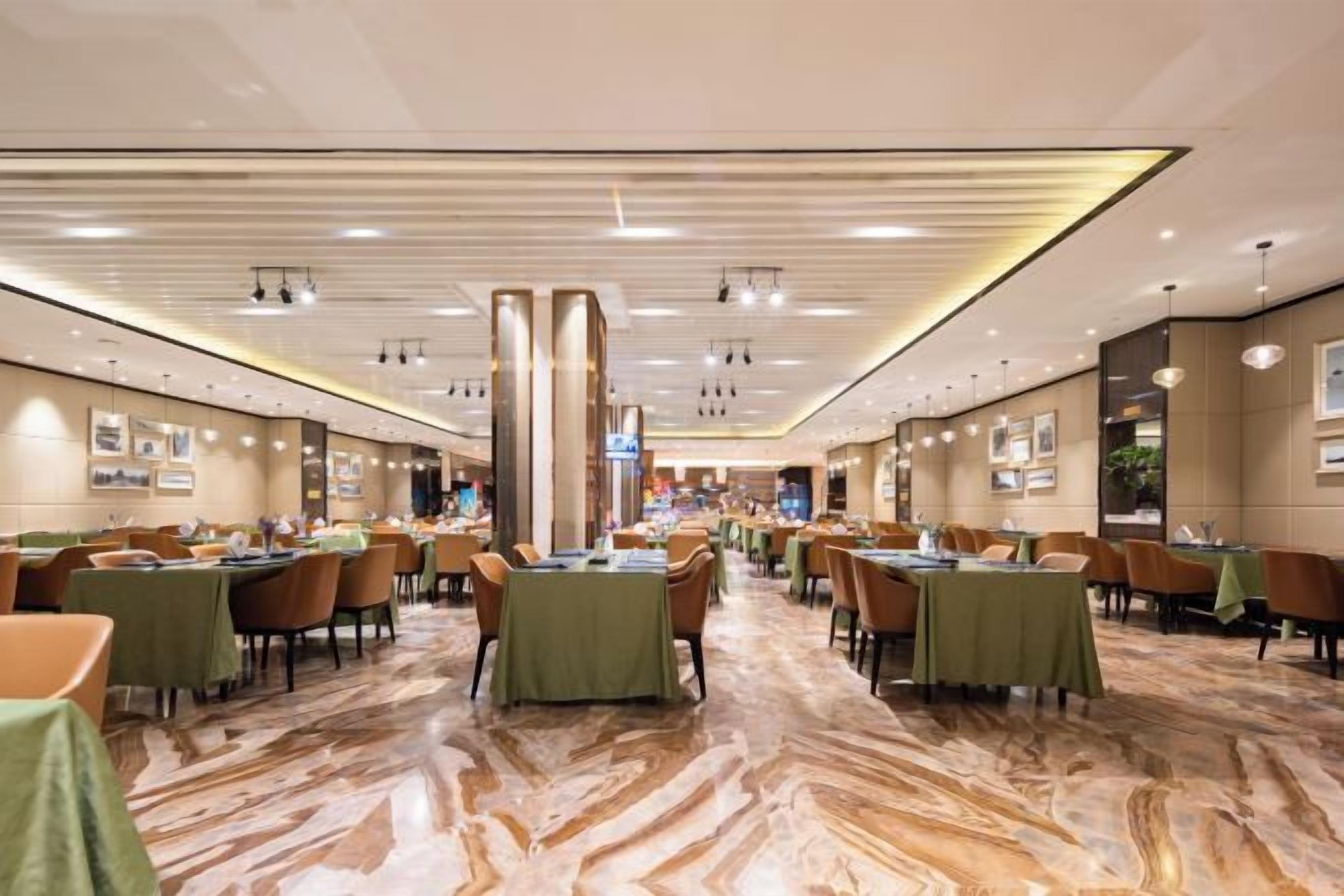 Ein geräumiger Hotel-Speisesaal mit mehreren Tischen und Stühlen, einem Marmorboden und einem modernen Deckenstil.