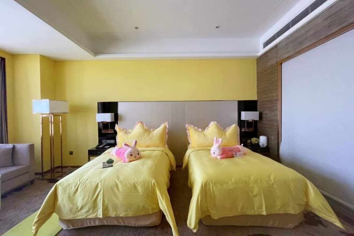 A hotel room with two beds, a sofa, a lamp, and a nightstand.