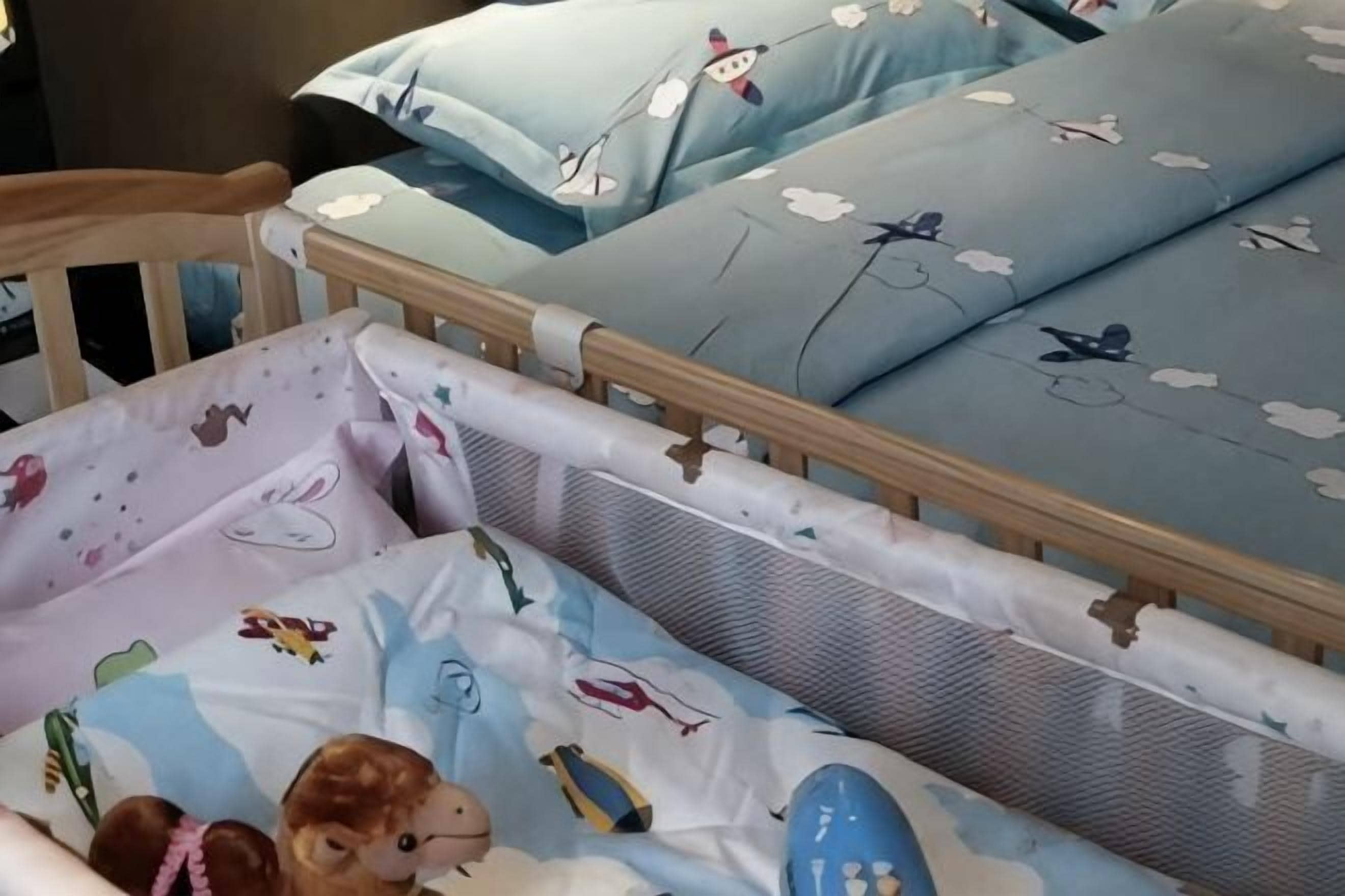 Una cama infantil con estructura de madera, colchón y almohadas con un estampado de cielo y nubes.