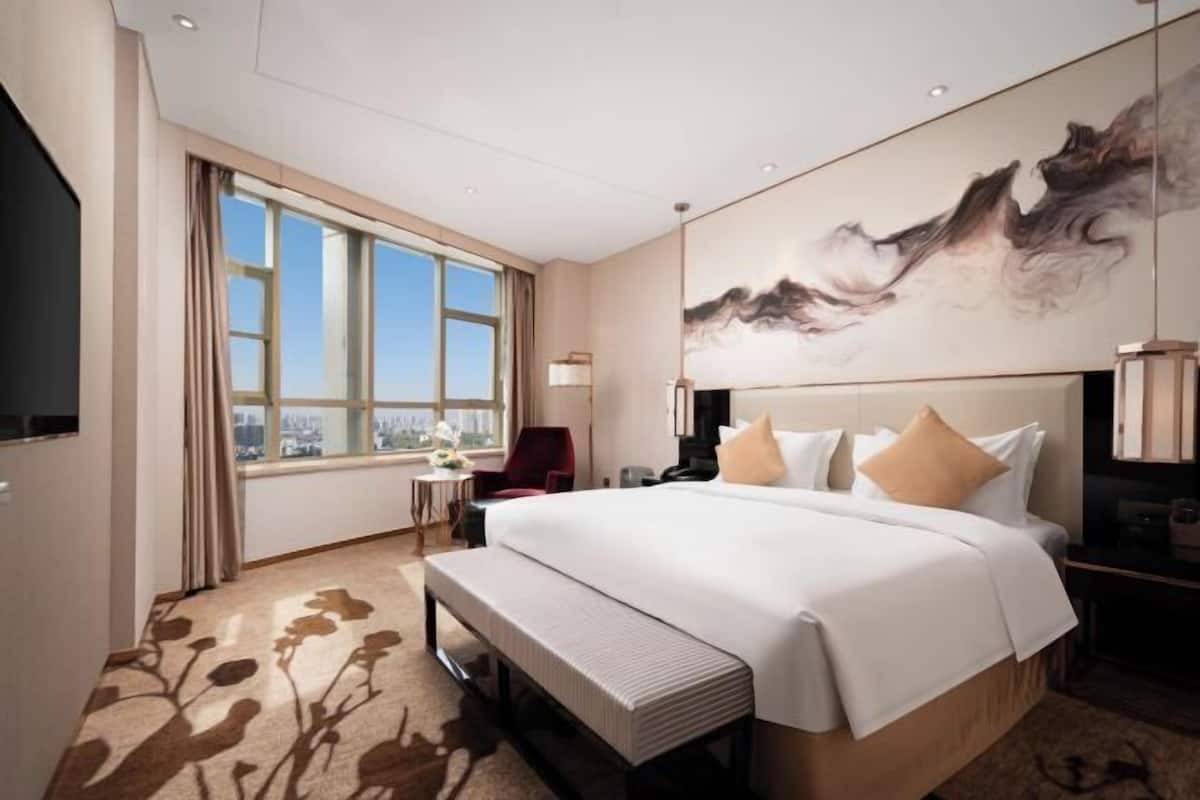 A hotel room with a large bed, a desk, a chair, a TV, and a window with curtains.
