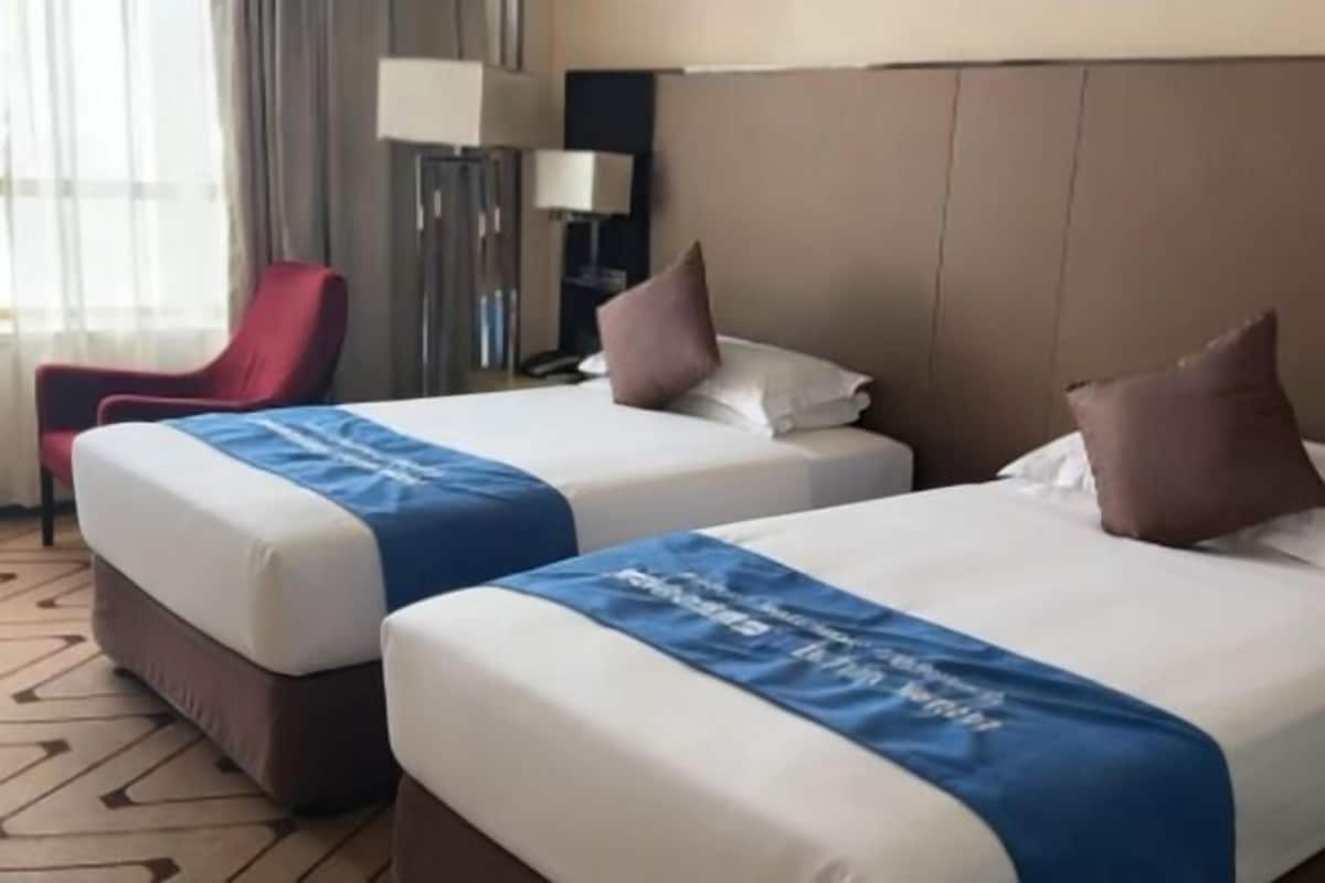 Two twin beds with blue bedspreads, a red chair, a lamp, and a patterned carpet.