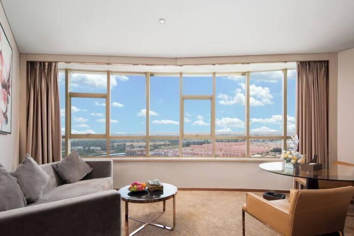 A modern hotel room with a large bay window offering a city view.