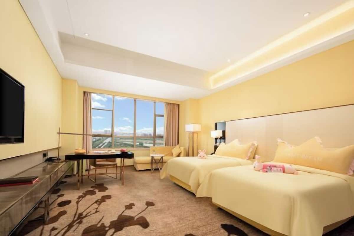 A hotel room with two beds, a desk, a chair, a TV, and a large window.