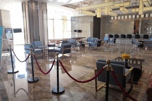 Un hall d’entrée spacieux au design moderne, avec un sol en marbre, des espaces de détente bleus et une barrière rouge faite de cordes.