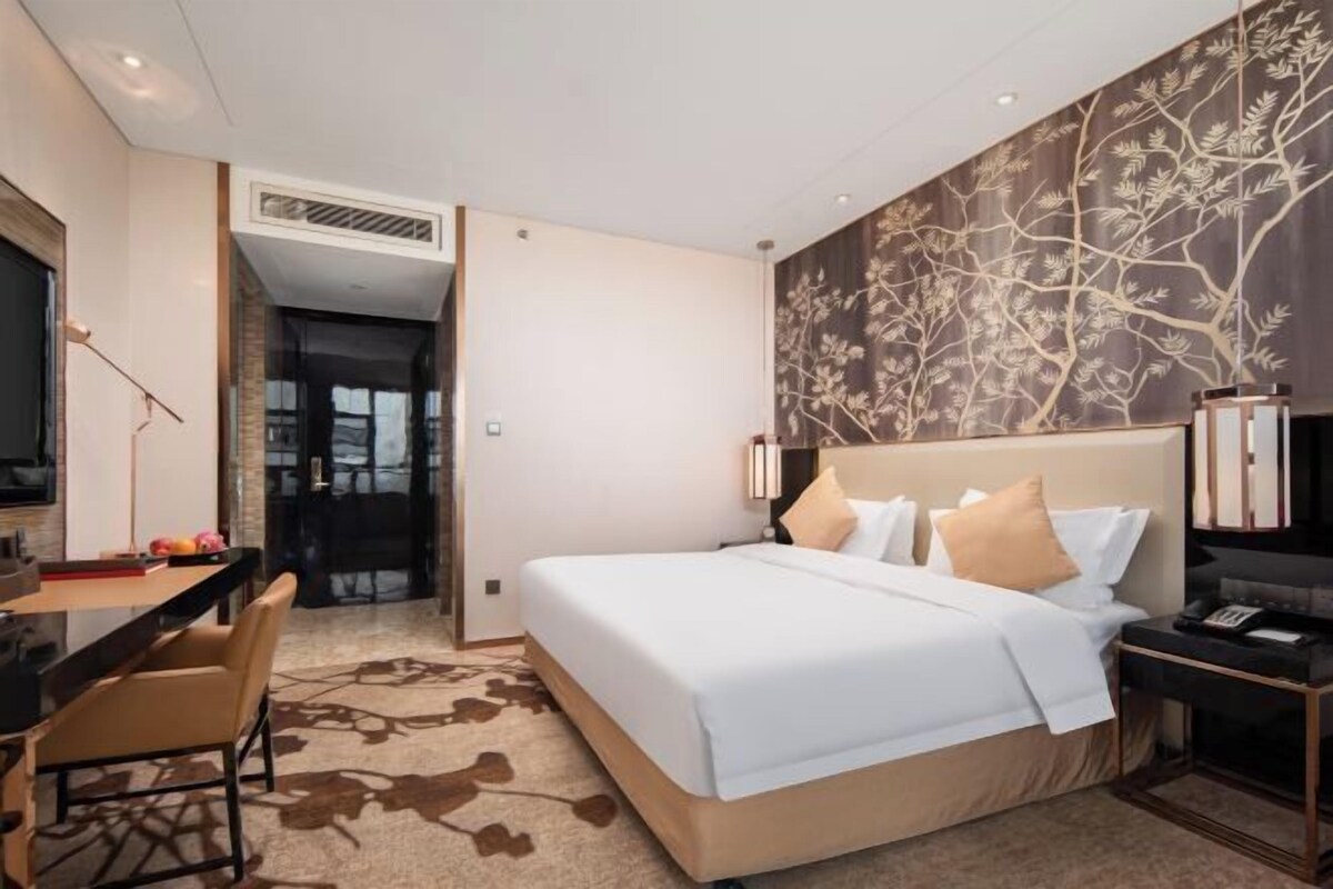 Une chambre d’hôtel avec un grand lit, un bureau avec une chaise, une télévision et un mur décoratif.