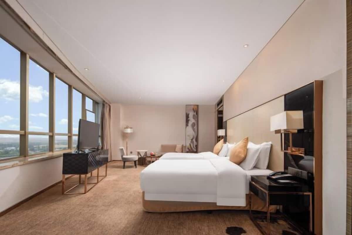 A modern hotel room with a large bed, a desk, a chair, a TV, and a view of the city.