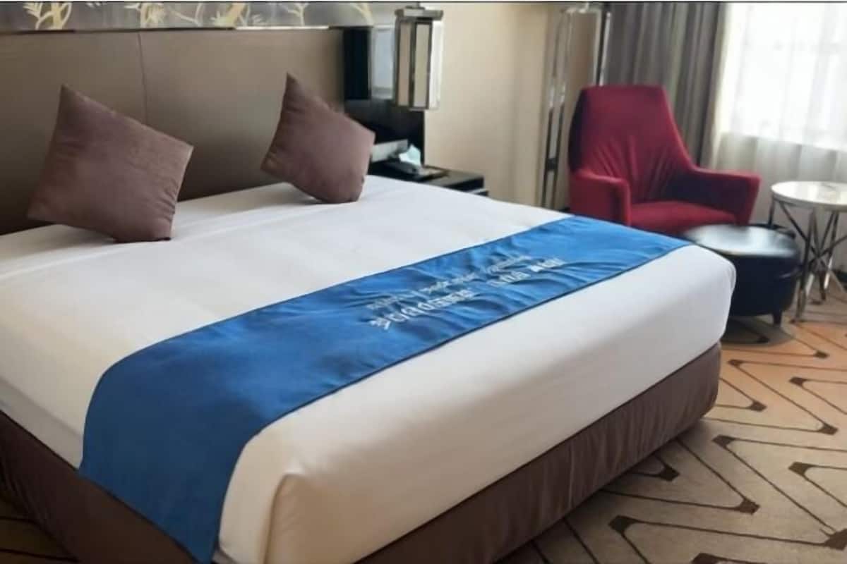 A hotel room with a bed, pillows, a red chair, a small table, and a lamp.
