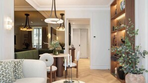 A modern living room with a sofa, a coffee table, and a dining area with chairs and a table. There are pendant lights above the dining table and a bookshelf with decorative items. - The Lander - Serviced 2BR/2BA - Opéra I (Paris)