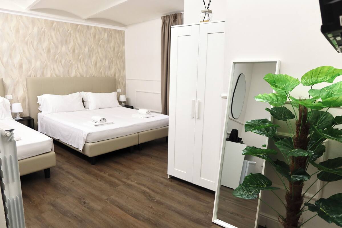 A hotel room with a bed, bedside tables, a wardrobe, and a large mirror.