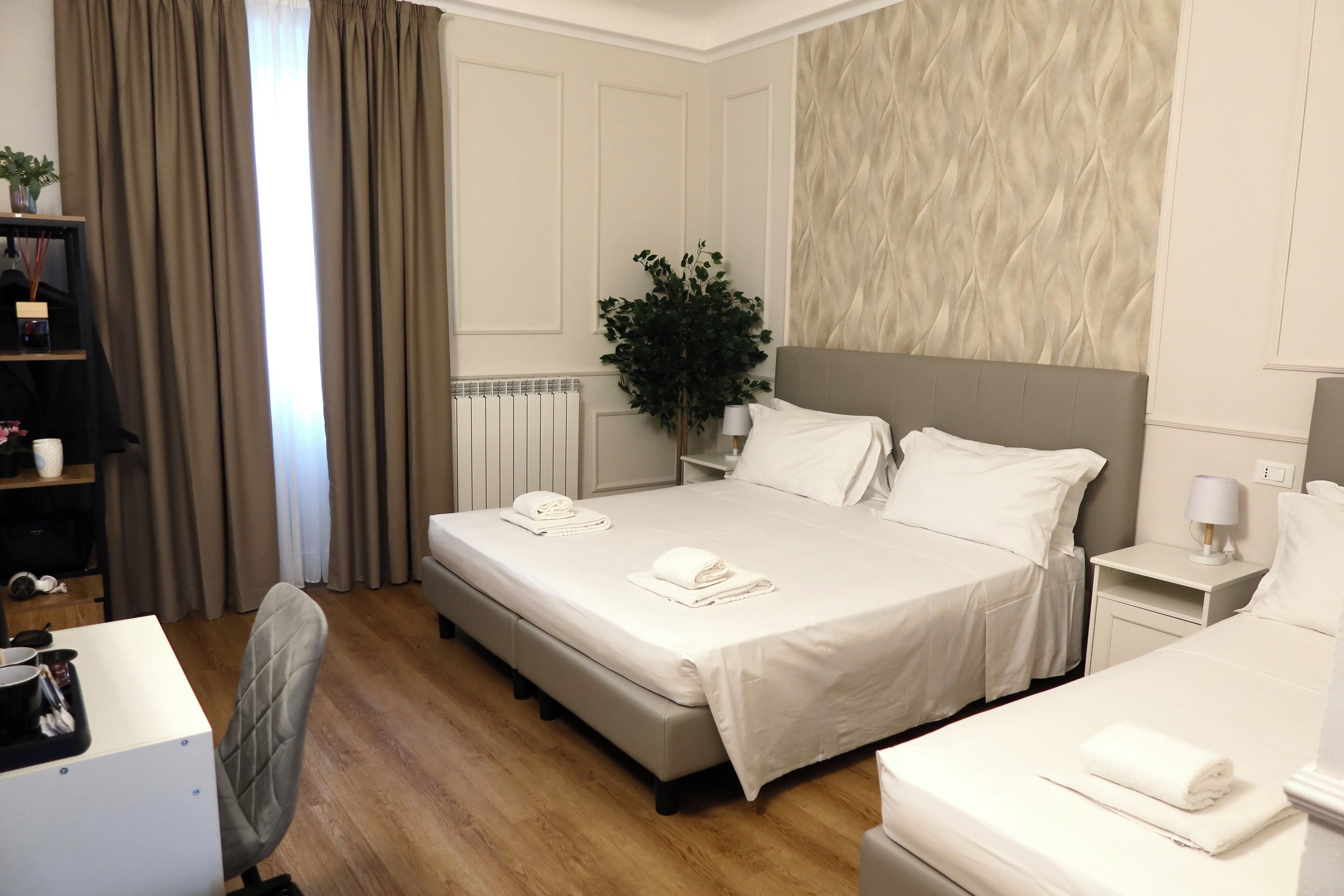 Ein Hotelzimmer mit zwei Betten, einem Schreibtisch, einem Stuhl, einem Heizkörper und einer Zimmerpflanze.