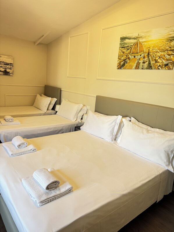 Habitación de hotel con dos camas individuales, cada una con ropa de cama y toallas blancas, un cabecero y un cuadro de un paisaje urbano en la pared.