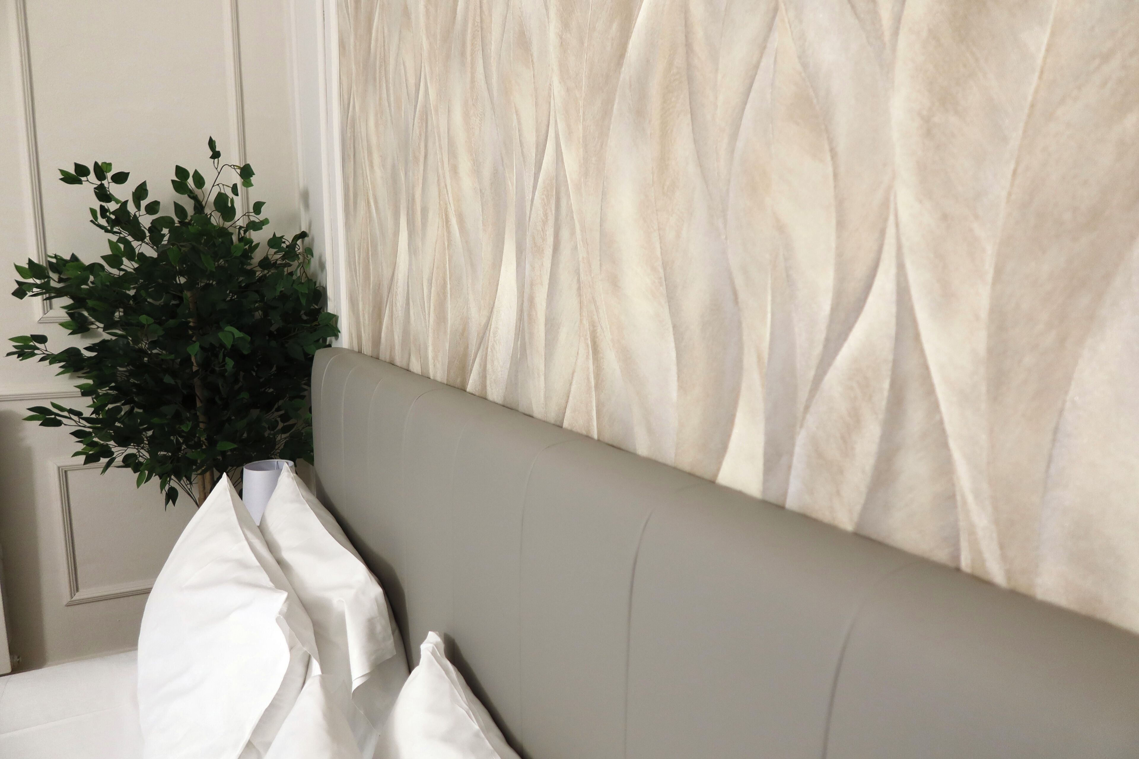 A bed with a grey headboard, white pillows, and a green plant beside it.