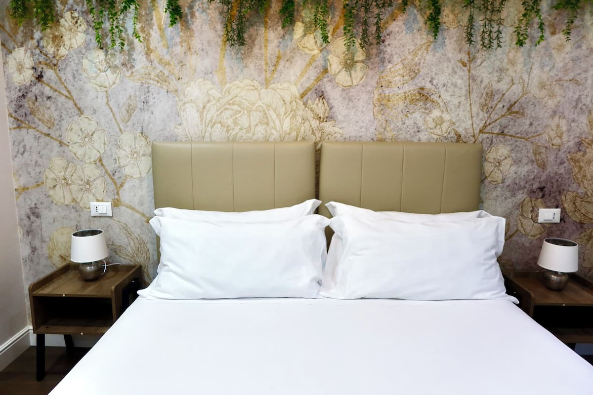 A neatly made bed with white linens, two bedside tables with lamps, and a floral wall mural.
