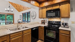 A kitchen with wooden cabinets, a stainless steel sink, a black stove, and a microwave.