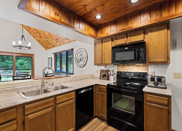 A kitchen with wooden cabinets, a stainless steel sink, a black stove, and a microwave.