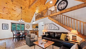 A spacious living area with a wooden ceiling, a staircase, a dining area, and a kitchen.