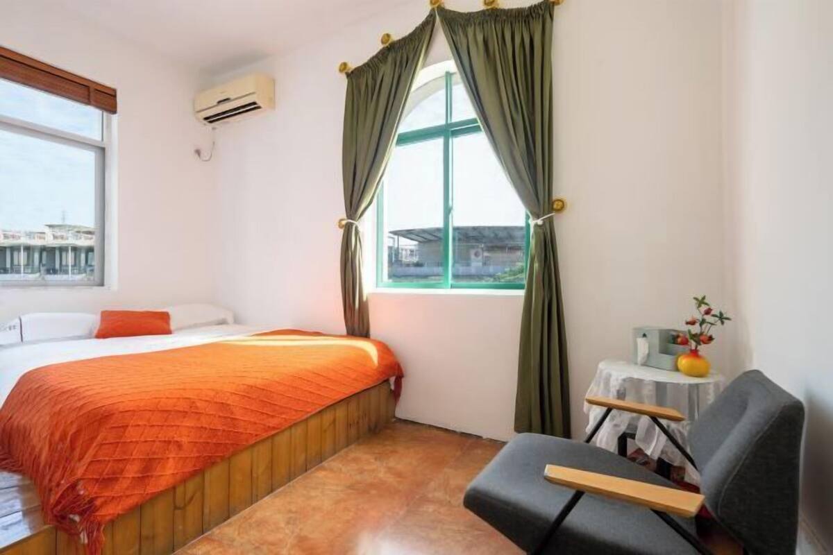 Una habitación de hotel con una cama, una silla, una mesita con un jarrón y una ventana con cortinas.