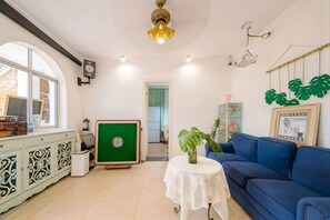Een woonkamer met een blauwe bank, een groene kast, een witte tafel met een vaas en een plafondventilator.