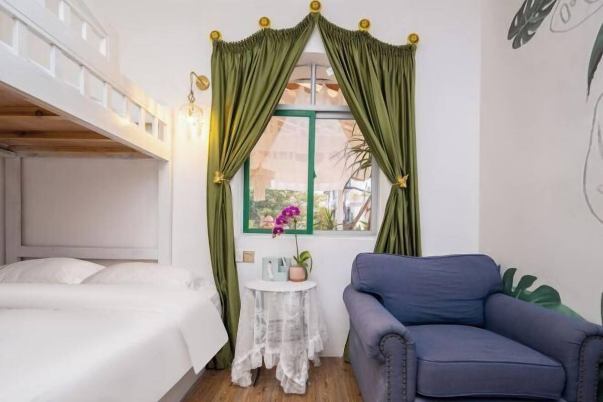 Una habitación con una cama litera, una mesita con una planta, un sofá y cortinas verdes.