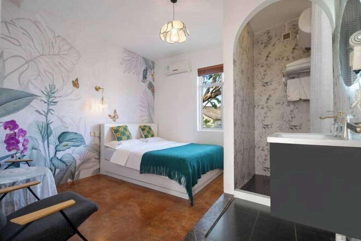 Un dormitorio con cama, ventana, baño con lavamanos y pared decorada con motivos de hojas.