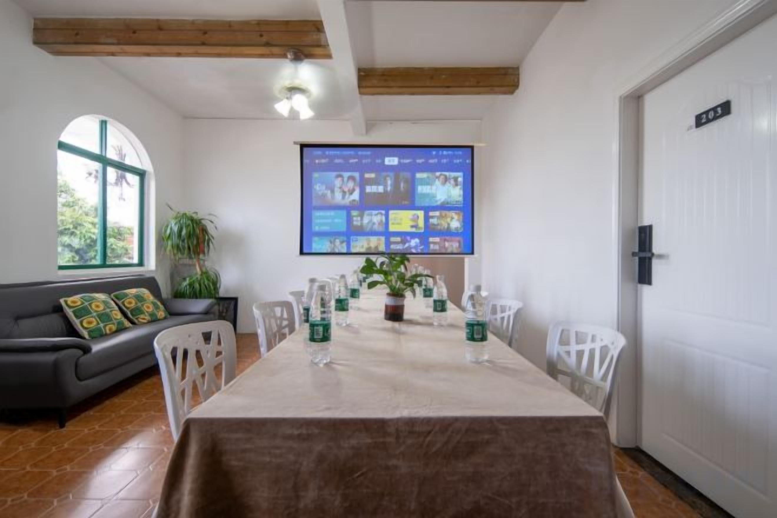 Un comedor con una mesa larga, sillas, una pantalla de proyector y un sofá con cojines.