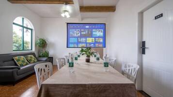 Un comedor con una mesa larga, sillas, una pantalla de proyector y un sofá con cojines.