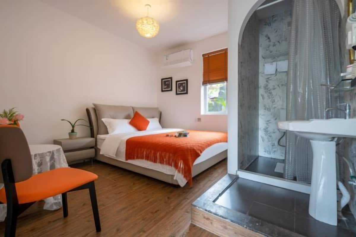 Un dormitorio con cama, una silla, una mesa y un baño con lavabo y ducha.