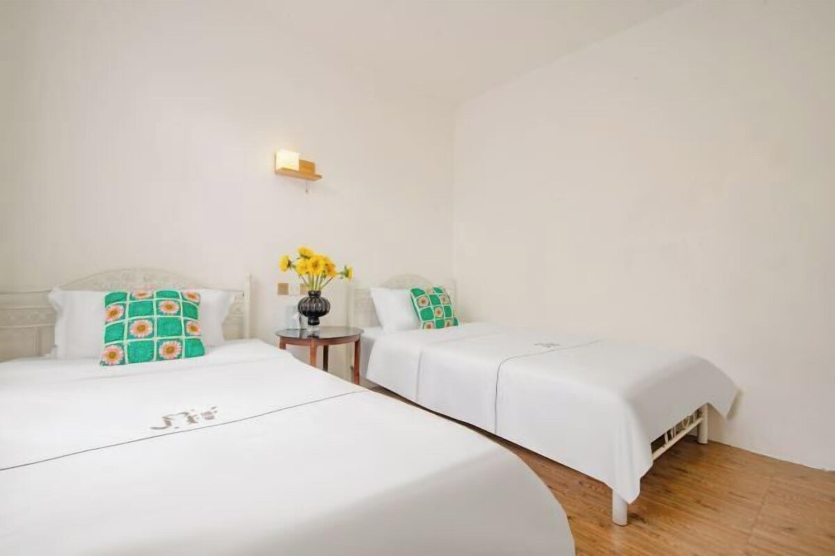 A hotel room with two beds, a small table with a vase of flowers, and a wall-mounted light fixture.