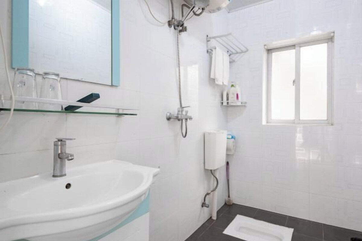 A bathroom with a white sink, a mirror, a shower, and a window.