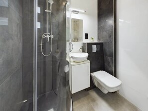 Un baño moderno con cabina de ducha de vidrio, un lavabo blanco y un inodoro.