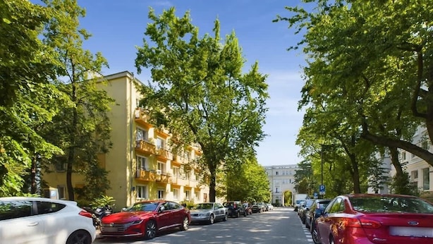 Calle bordeada por coches estacionados y árboles, con edificios a ambos lados.